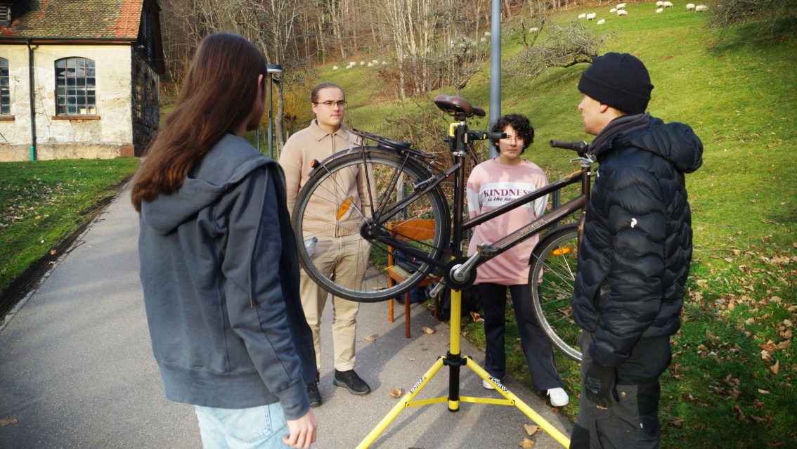 Drei junge Menschen auf einem kleinen Fahrweg, zwischen ihnen ein Fahrrad auf einem Montageständer