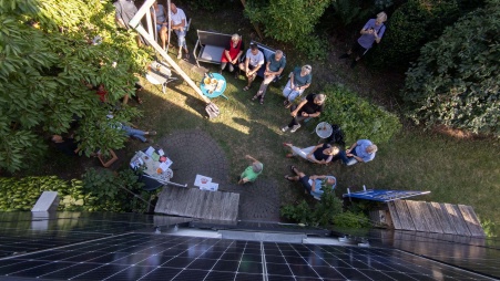 Blick von oben auf eine Gruppe Menschen, die sich um eine mit PV-Modulen bestückte Hauswand schart