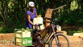 Eine Schwarze Frau mit einem beladenen E-Bike der Marke AfricroozE vor Bäumen