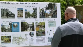 Ein glatzköpfiger Mann mit Sonnenbrille steht im Freien an einer Straße und studiert, von der fotografierenden Person abgewandt, eine Wandzeitung zum Thema Kiezblocks.