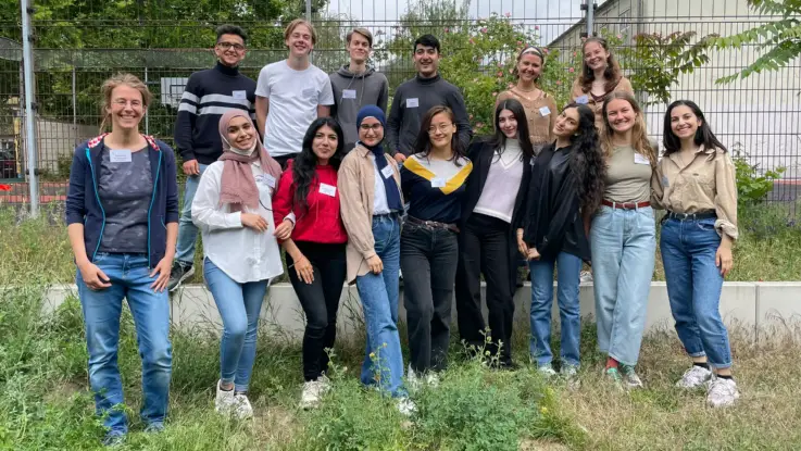 Eine Gruppe junger Menschen hat sich am Rande eines Sportplatzes zum Foto aufgestellt.