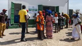 Vor einem neu errichteten Kühlhaus eine Gruppe bunt gemischter Einwohner:innen eines Dorfes in Gambia