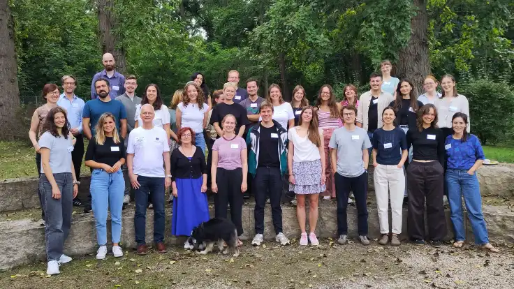 Eine Gruppe von gut 30 jungen Erwachsenen in legerer Kleidung hat sich zum Gruppenfoto vor einem Wald versammelt