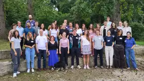 Eine Gruppe von gut 30 jungen Erwachsenen in legerer Kleidung hat sich zum Gruppenfoto vor einem Wald versammelt