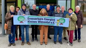 Vor einem Halleneingang hat sich eine Gruppe von 10 Bürger:innen versammelt, sie halten ein Banner mit dem Text «Erneuerbare Energien Kleines Wiesental e. V»