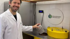 Ein Mann legt eine Plastkdose mit Pilen in einen tonnenförmigen Behälter mit Radioaktiv-Symbol