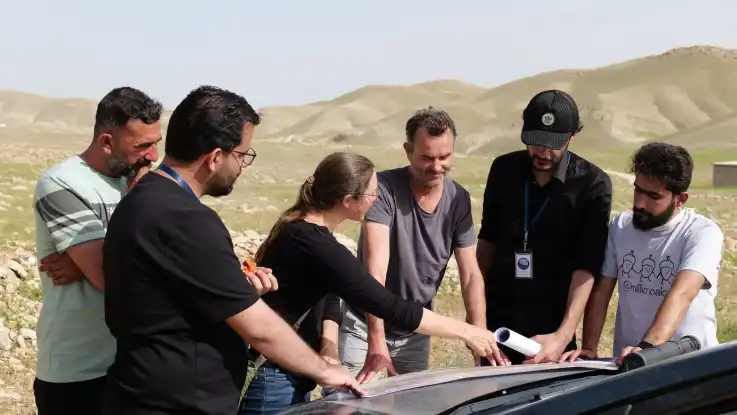 Eine Gruppe von Menschen vor einer wüstenartige Landschaft diskutiert über einen Plan.