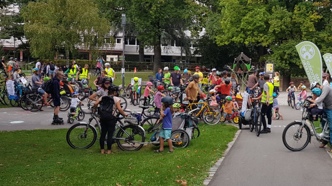 In einem Park versammelt sich eine große Gruppe vornehmlich junger Menschen mit Fahrrädern, darunter auch viele Kinder.