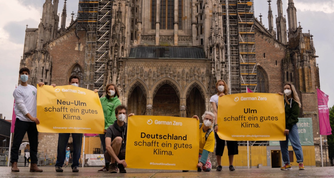 Vor dem Ulmer Münster präsentieren Klimaaktivist:innen Banner, die für Klimaentscheide in Ulm und anderswo werben.