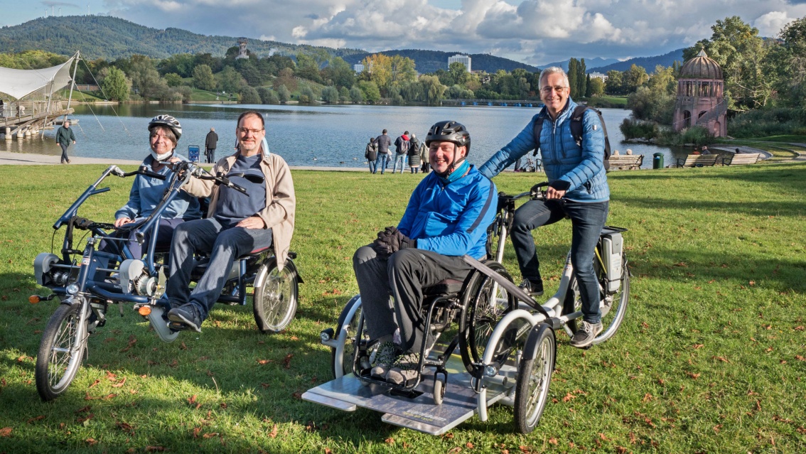 Vier Menschen mit Lastenrädern auf einer Wiese an einem idyllisch gelegenen See