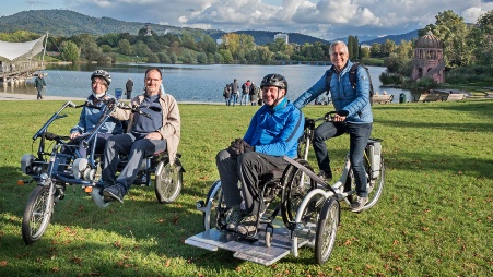 Vier Menschen mit Lastenrädern auf einer Wiese an einem idyllisch gelegenen See