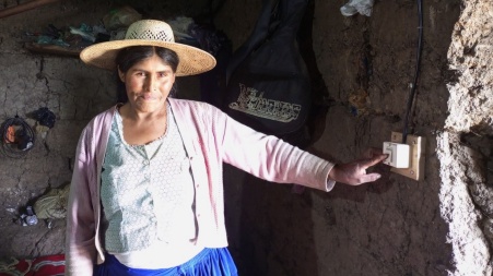 Eine bolivianische Bäuerin in einem kargen Schuppen, stolz betätigt sie einen Lichtschalter.