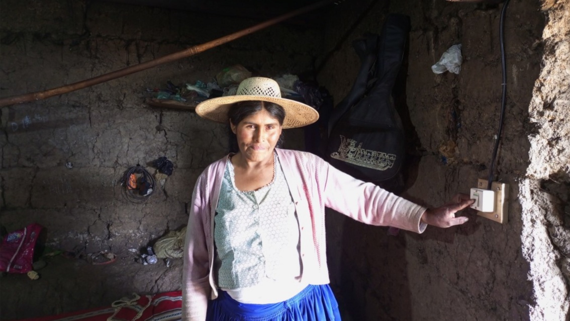 Eine bolivianische Bäuerin in einem kargen Schuppen, stolz betätigt sie einen Lichtschalter.