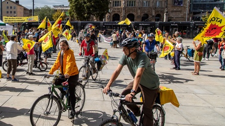 Teilnehmende an einer Fahrraddemo auf dem Platz vor dem Theater Freiburg, sie haben viele Flaggen mit der Anti-Atom-Sonne dabei.