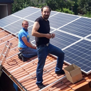 Ralf von der Langes Sohn steht auf dem Dach einer Garage, hinter ihm der Vater, der von seiner Arbeit an einem Solarmodul aufblickt.